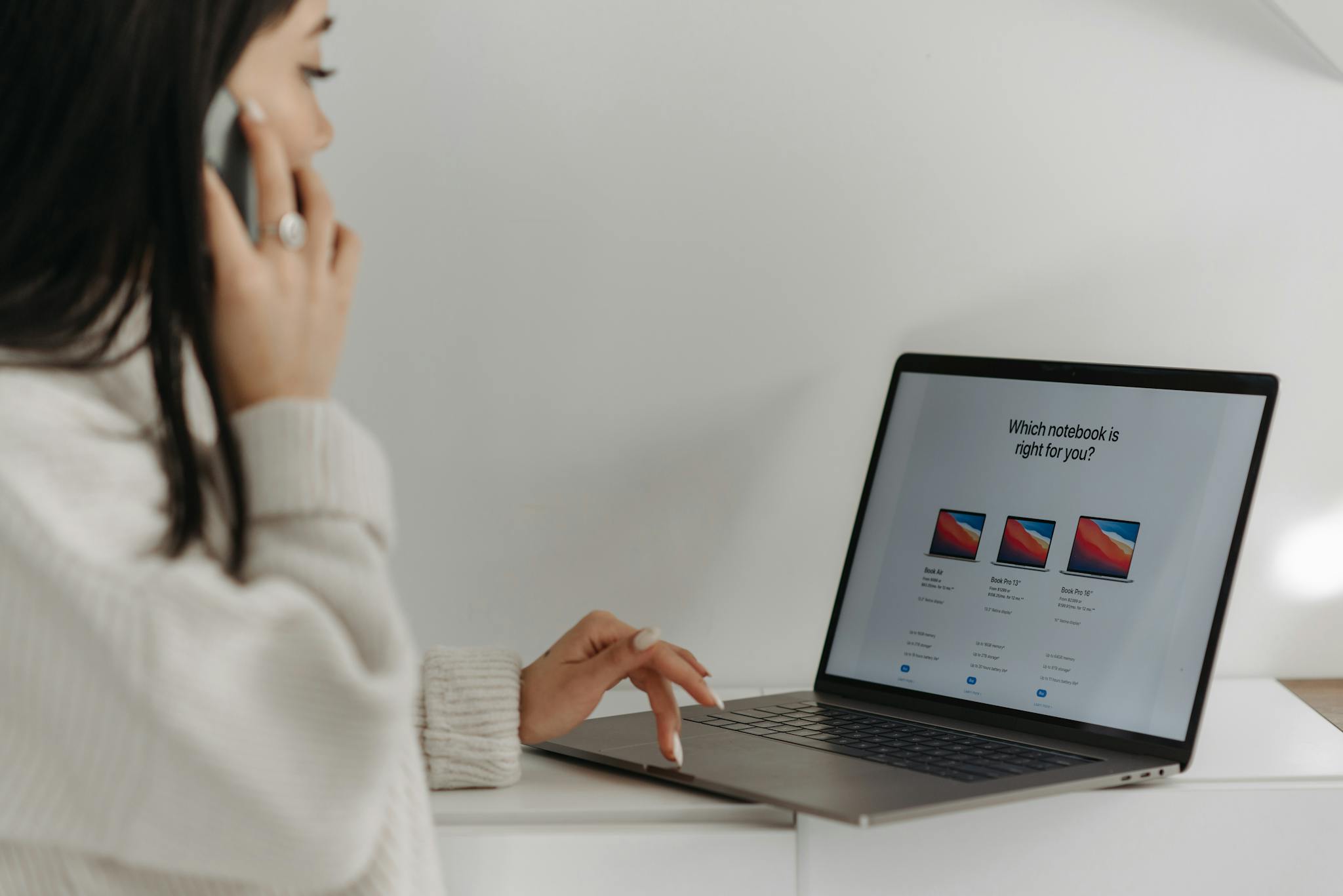 Asian woman on phone using laptop for online shopping against a white wall.