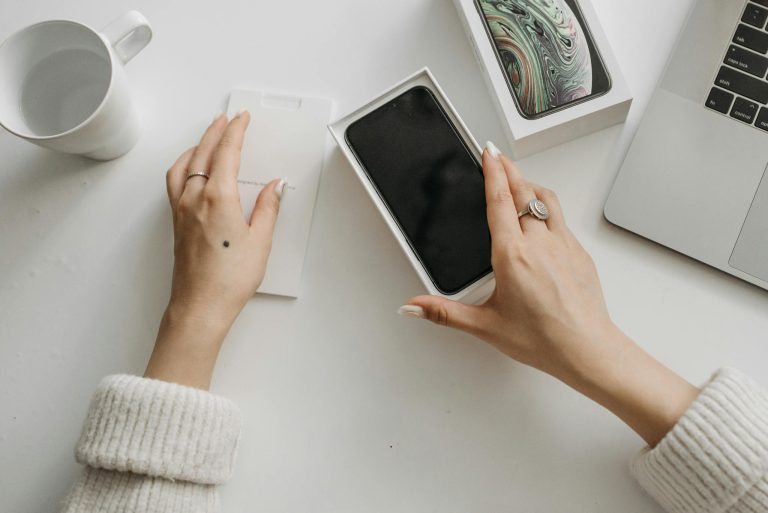 Woman unboxing a smartphone on a white table, showcasing technology and lifestyle