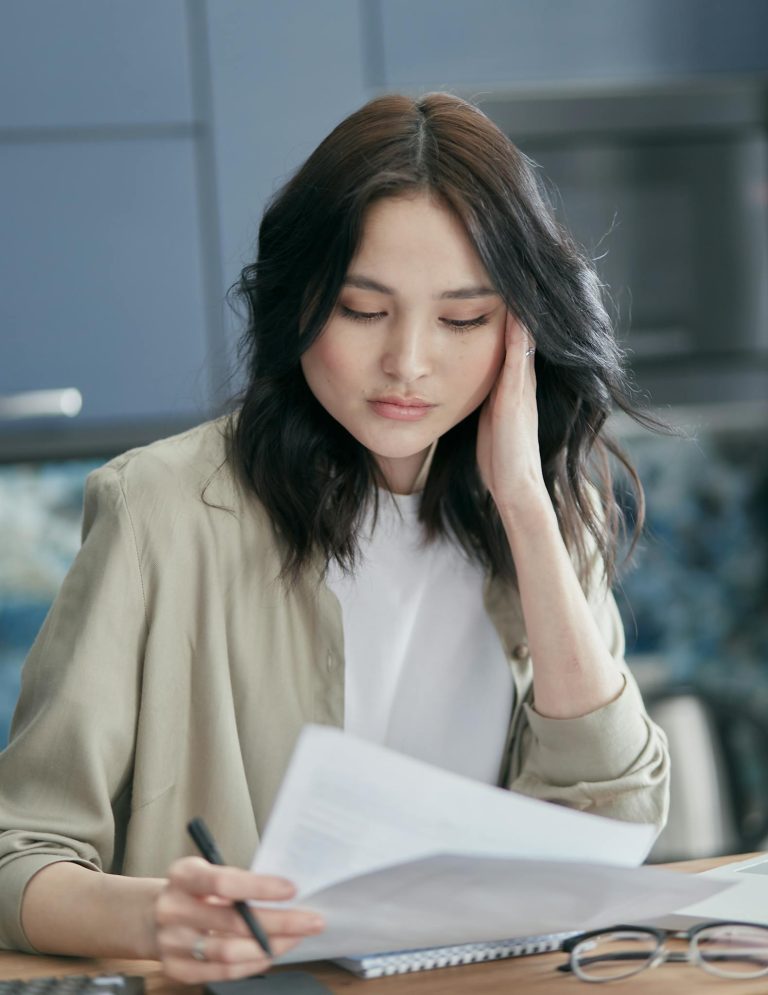 Young woman reviewing paperwork at home, focused and concerned.